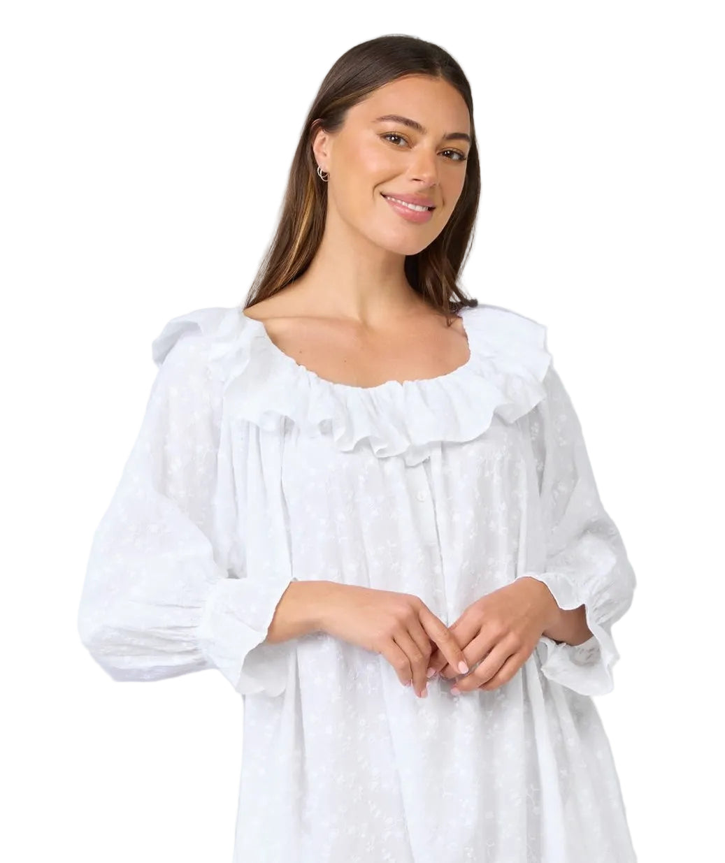 A woman wearing a white long-sleeve nightgown with a ruffled neckline, photographed against a solid light gray studio background.