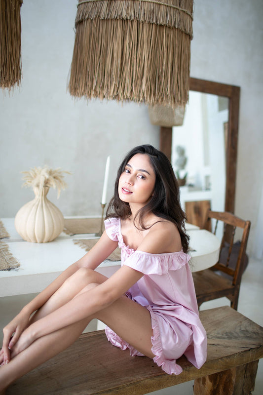 Young woman wearing a pearl pink Pyjama set. Shorts have ruffle and pocket, top has ruffle shoulder straps