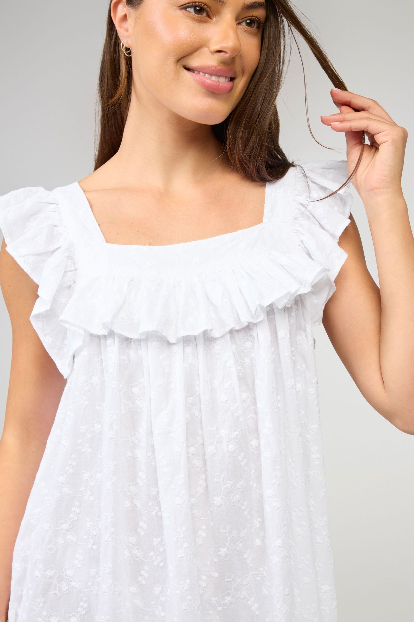 Woman wearing a white dress with ruffled details against a plain background