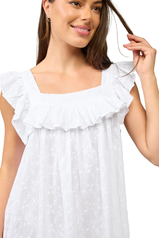 Woman wearing a white dress with ruffled details against a plain background