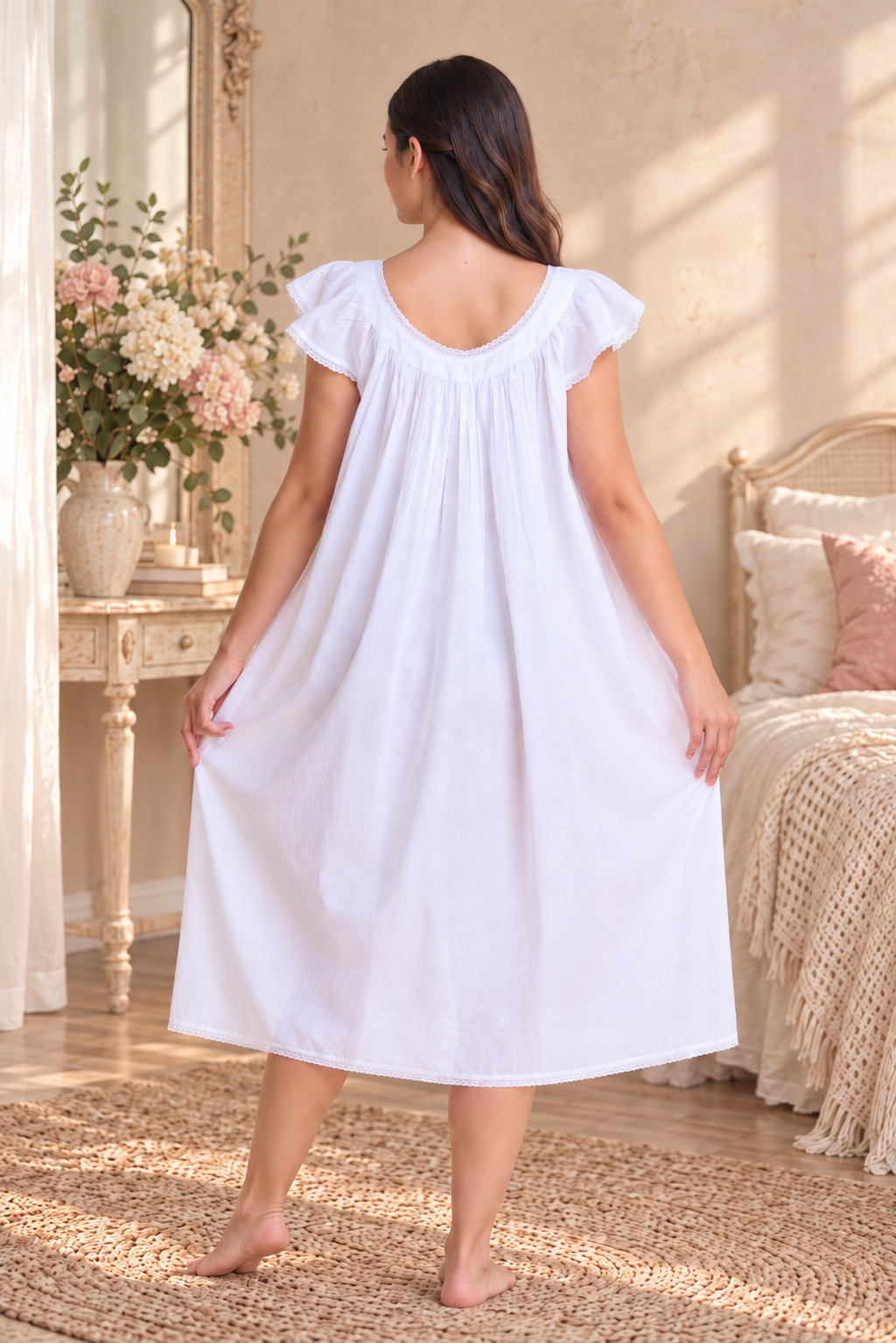 A woman stands barefoot in a softly lit bedroom, viewed from the back, wearing a loose white nightgown with ruffled cap sleeves and a gathered neckline.