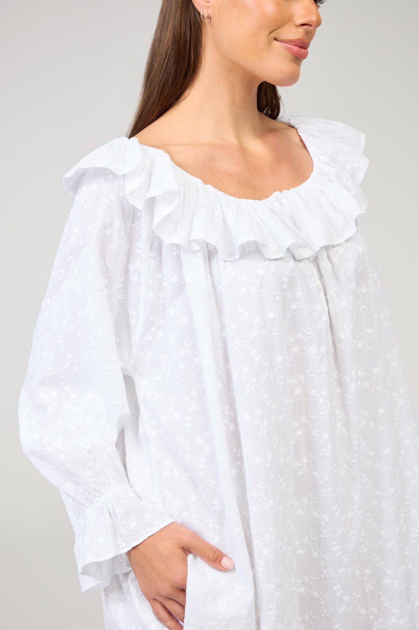 Woman wearing a white blouse with ruffled details on a plain background