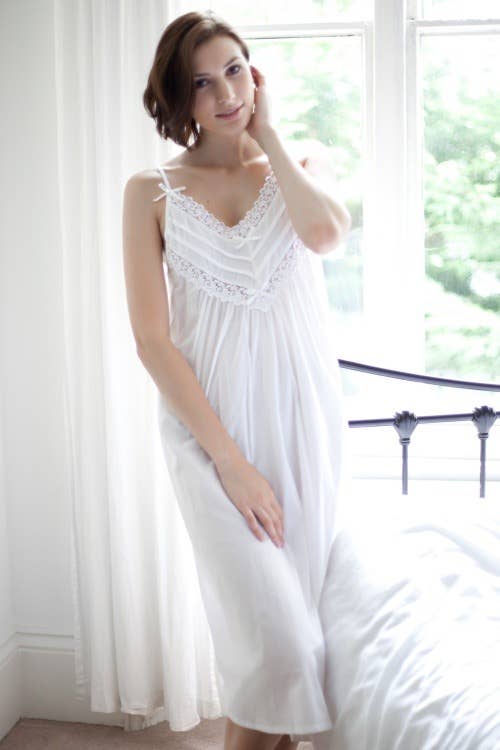 CAI Victorian Style Ladies Cotton Strappy Nightdress is made of 100% Cotton Lawn. It has a V neck cross pleating detail across the yolk and is trimmed with soft floral lace and bow detail. The nightie gathers gently under the bust line, is elasticated under the arms for comfort and falls  slightly flared creating a stunning silhouette