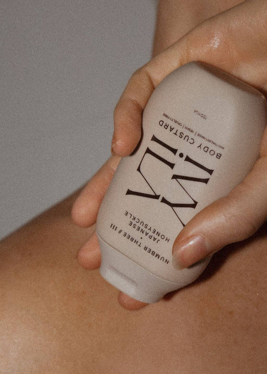 Hand holding a beige body butter container with branding on a neutral background