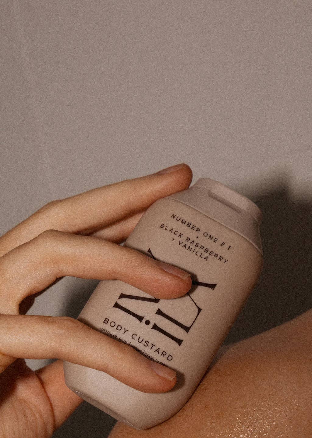 Hand holding a beige bottle labeled 'Body Custard' against a neutral background
