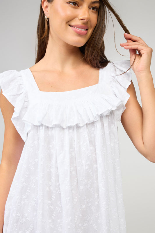 Woman wearing a white dress with ruffled details against a plain background