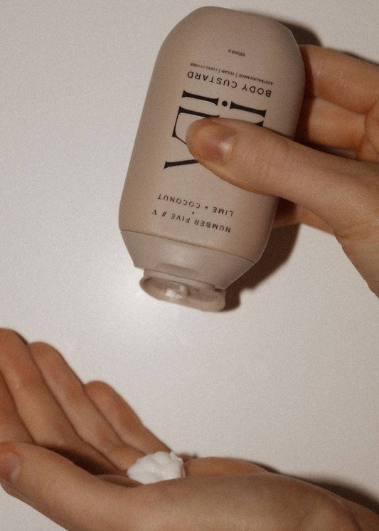 Hand holding a beige bottle labeled 'Body Gusto' with a small amount of cream on the palm.