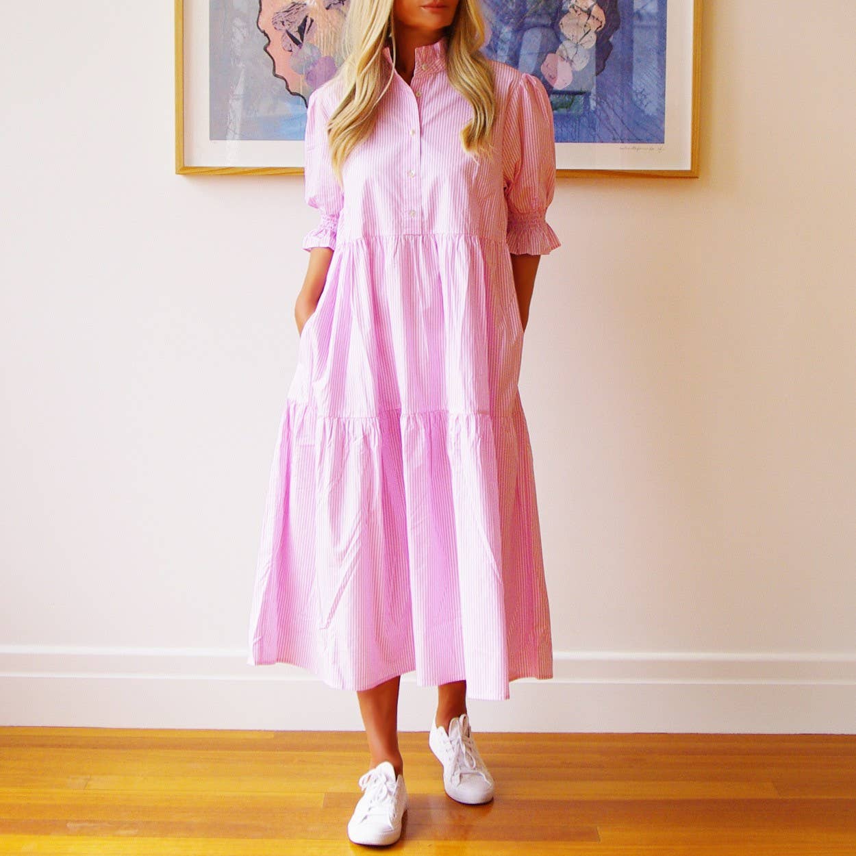 Woman wearing a pink dress standing in a room with a framed picture on the wall.