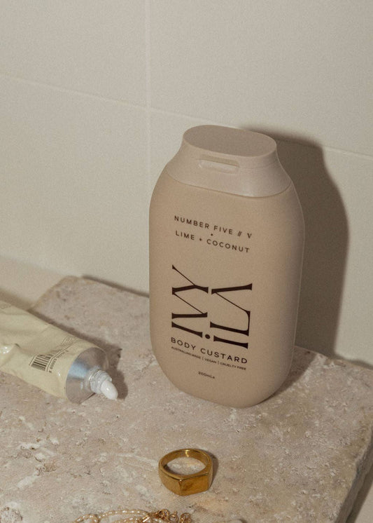 Beige bottle labeled 'Milky' on a bathroom counter with a gold ring and tube of cream.