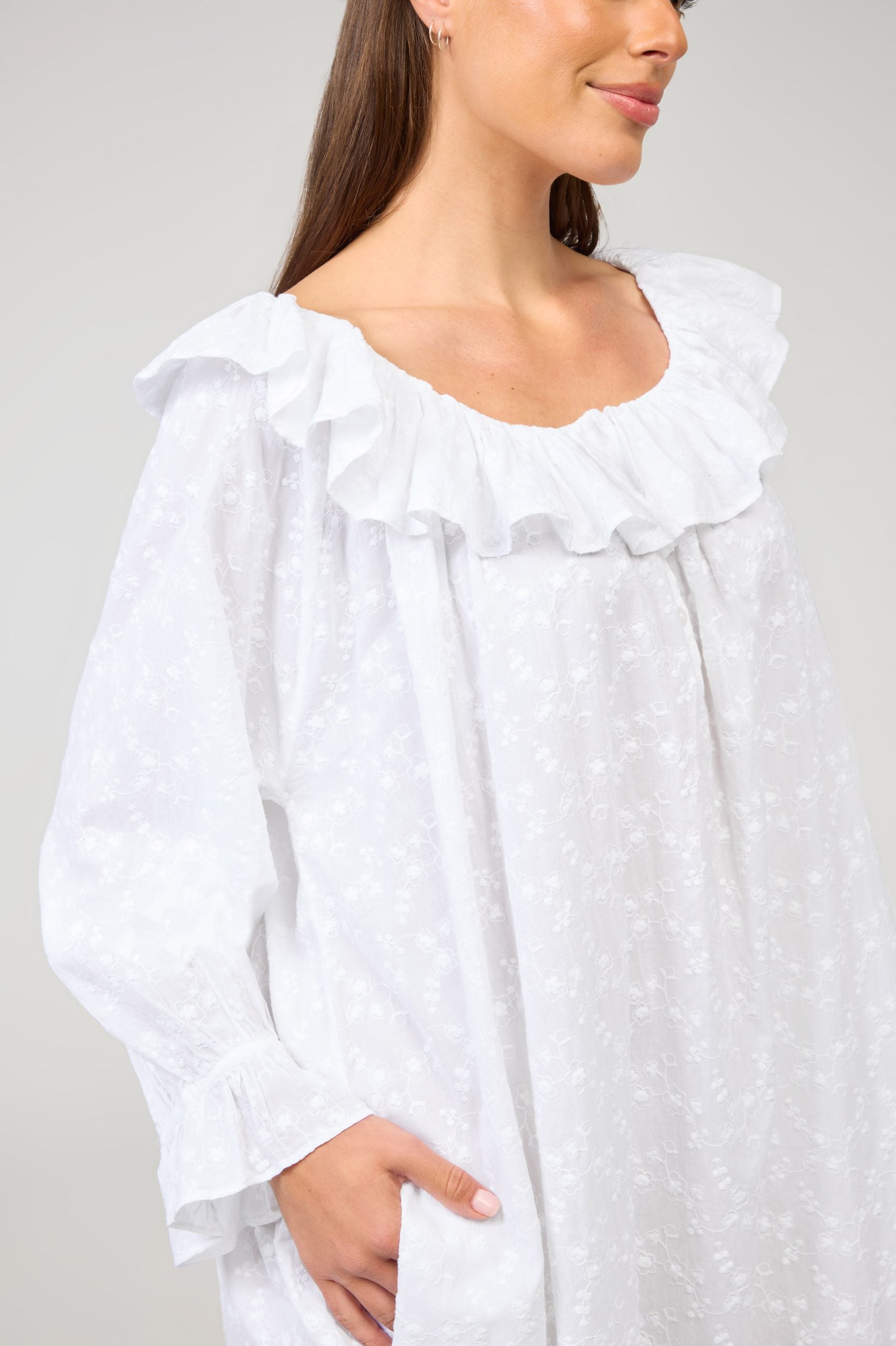 Woman wearing a white blouse with ruffled details on a plain background