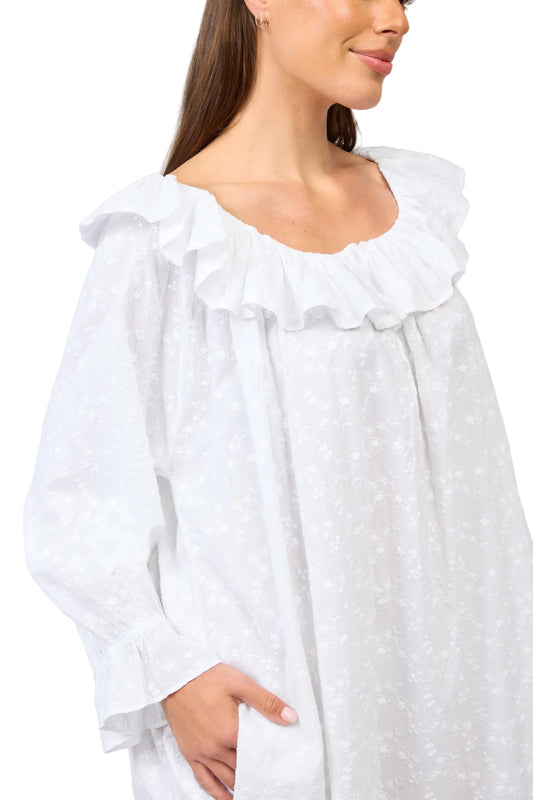 Woman wearing a white blouse with ruffled details on a plain background